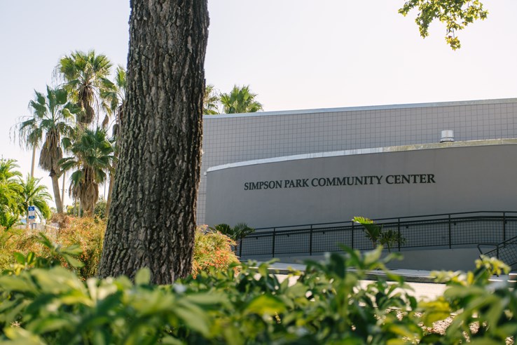 Front of the Simpson Park Community Center, with the name on the side of the builiding. Tree and plants in forefront.