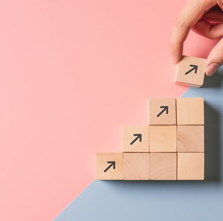 stock photo of wooden squares being stacked leading up with arrows painted on outside squares and a hand placing them on top of one another