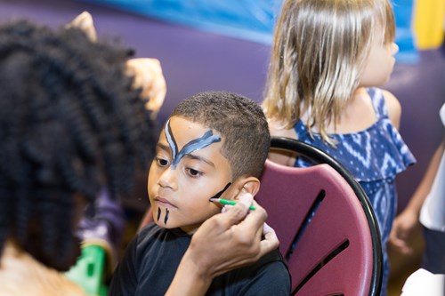 foreground: boy getting face paint. Background: another child waits for her turn.