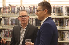 Two people conversing at the Lakeland History and Culture Center opening reception, standing in front of library shelving for DVDs