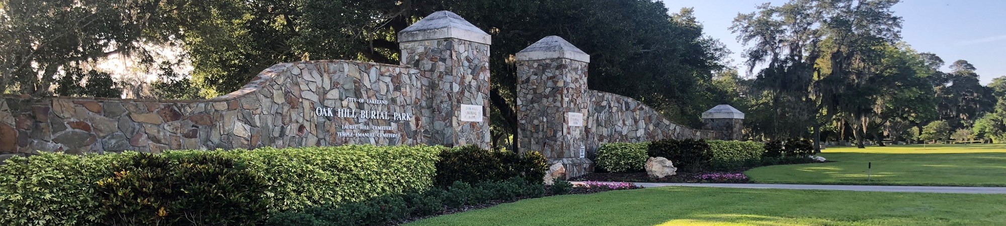 Photo of the gates at the front of Oak Hill Cemetery. There are two stone pillars with stone walls on either side and a small opening to the cemetery between them.