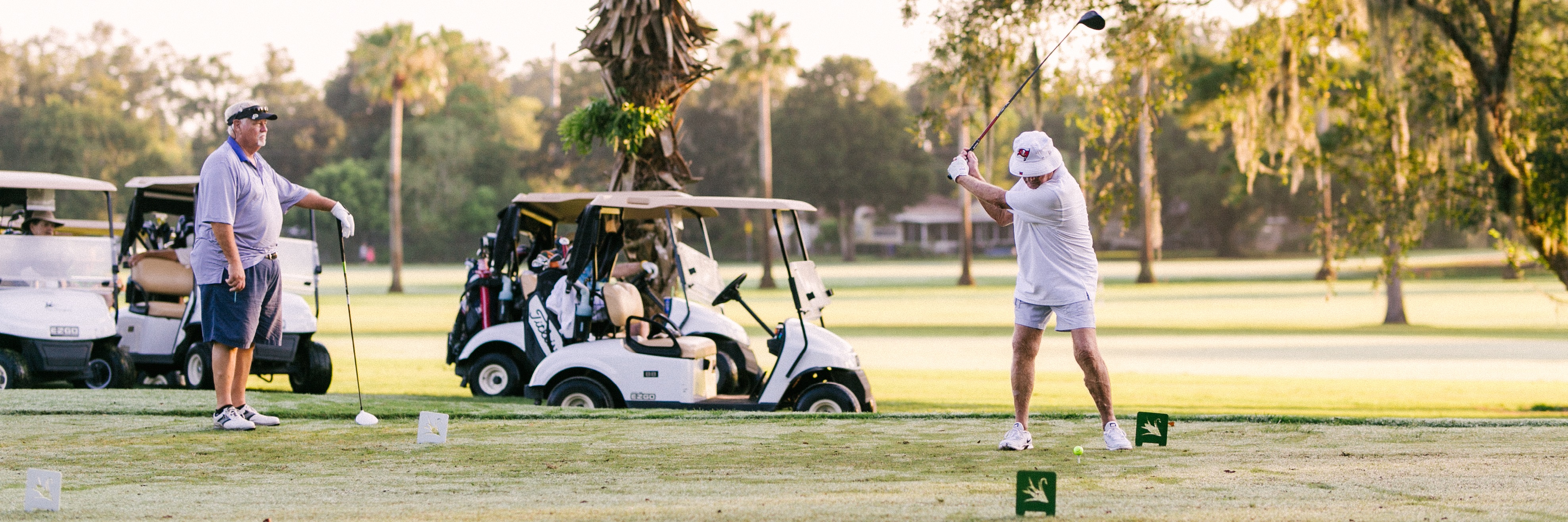 Photo of Cleveland Heights Golf Course with man swinging golf club and two golf carts in the background.