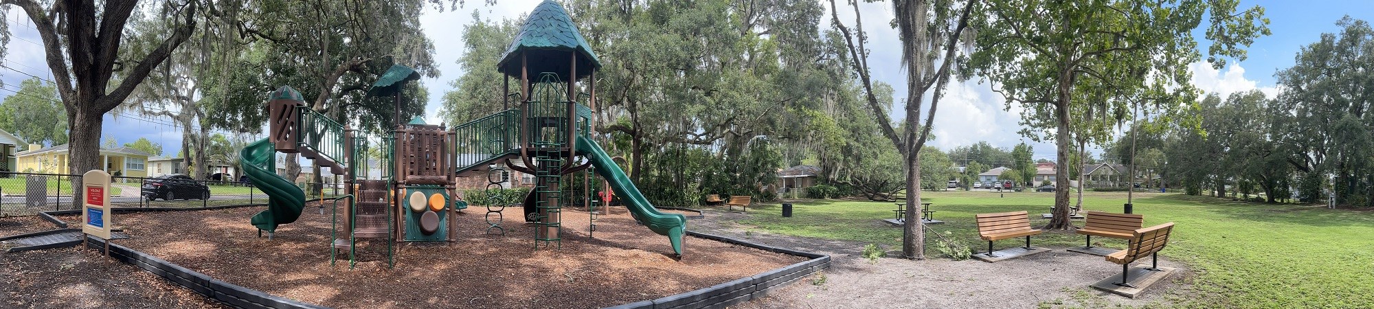 Photo of Horney Park. Picture features a playground set on the right and a grassy field with a bench on the left.