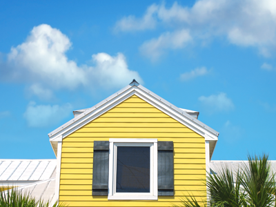 A yellow house with one window stands against a bright blue sky. 
